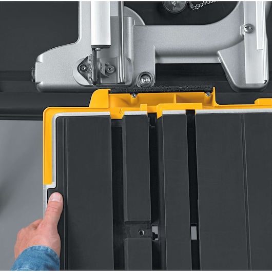 Close-up of a hand adjusting a DEWALT D24000 tile saw table with yellow and black parts.