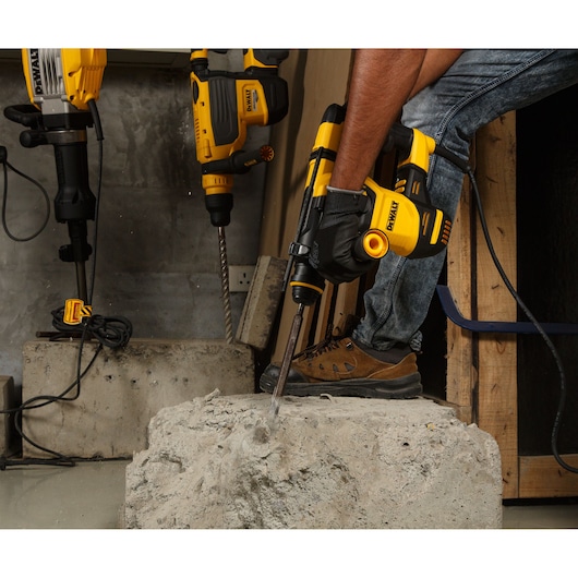 DEWALT rotary hammer in use drilling concrete, shown on a construction site with worker and other tools.