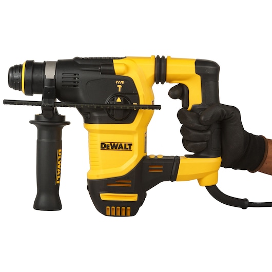 A DEWALT branded yellow and black rotary hammer drill, model D25333K, is held by a gloved hand. The drill has a side handle and visible adjustment controls.