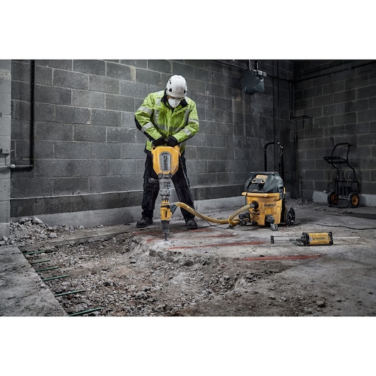 A person wearing protective gear operates a DEWALT D25911 demolition hammer on a concrete floor inside a construction site