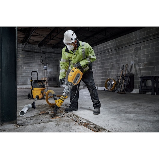 A construction worker wearing a helmet and high-visibility jacket uses a DEWALT D25911 demolition hammer to break concrete