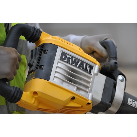 Close-up of a person holding a DEWALT demolition hammer, showing the yellow and black tool with gloved hands.