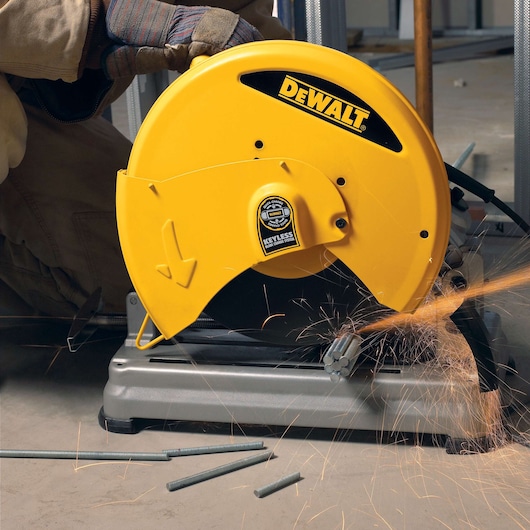 A DEWALT D28715 yellow metal cut-off saw in use, cutting metal rods and producing sparks, operated by a person wearing protective gloves.