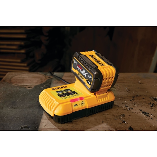 A DEWALT DCB117 yellow battery charger with an attached DEWALT XR FLEXVOLT 18V/54V battery, sitting on a dusty workbench.