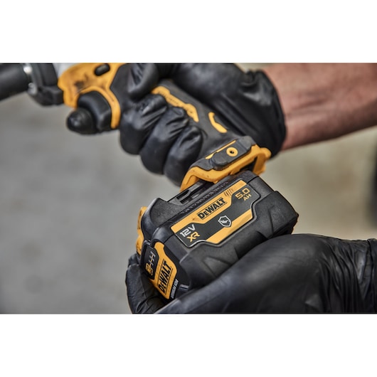 Close-up image of a person wearing black gloves holding and installing a DEWALT 12V XR 5.0Ah battery, model DCB126G, onto a compatible tool.
