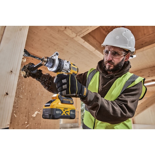 Person drilling wood with DEWALT XR 18V 8Ah cordless drill in a construction setting, wearing safety gear.