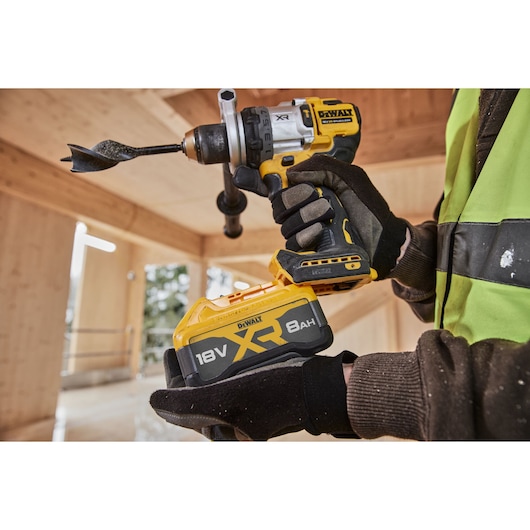 DEWALT 18V XR 8Ah battery shown with cordless drill held by gloved hands at a construction site.