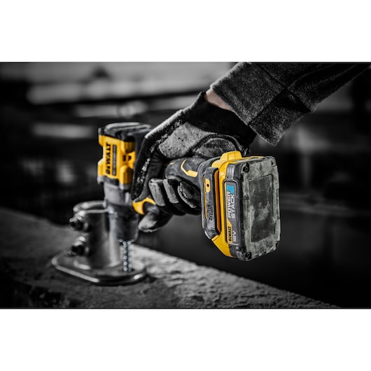 DEWALT Powerstack 18V battery attached to a cordless drill, used by a gloved hand on a construction site.