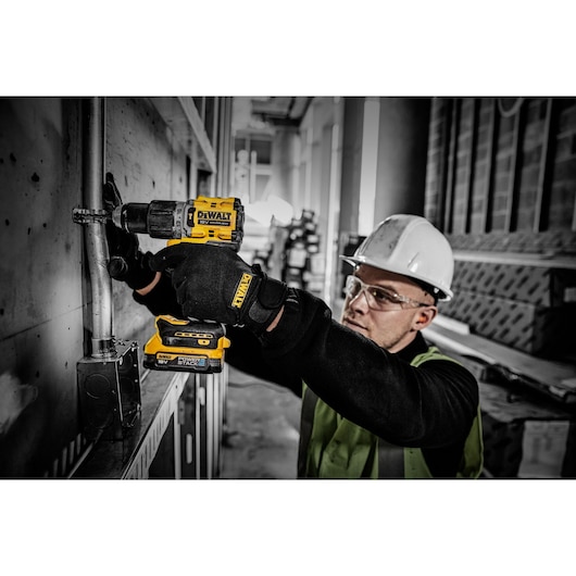 Worker uses DEWALT Powerstack battery in a cordless drill during electrical installation on an industrial site.