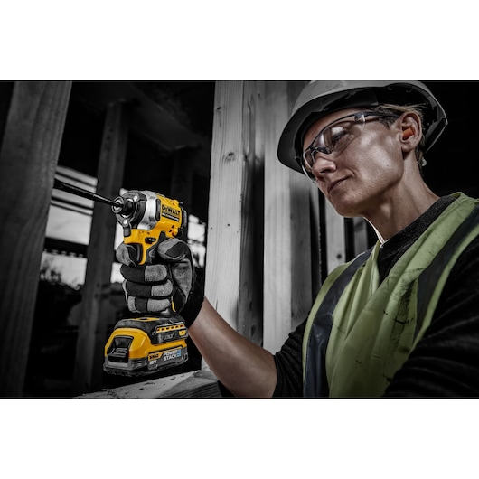 Worker using a DEWALT tool powered by DCBP034 battery at a construction site, face blurred for privacy.