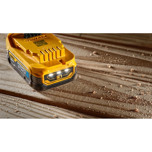 DEWALT 18V POWERSTACK battery with LED light, lying on a wooden surface with wood shavings.