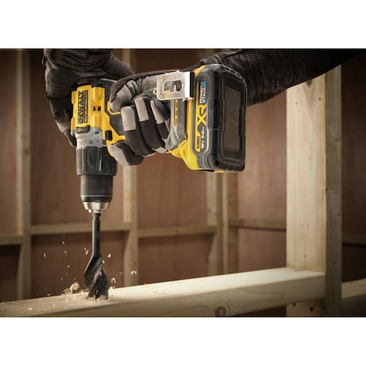 Close-up of a DEWALT drill with DCBP318 battery in use, drilling into wood at a construction site.