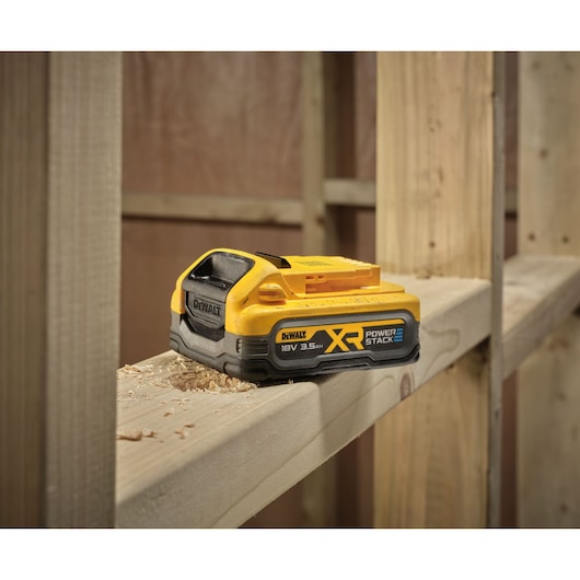 A DEWALT XR Power Stack 18V 3.5Ah battery is shown resting on a wooden beam in a construction setting.