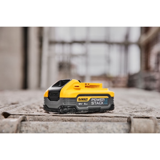 DEWALT POWERSTACK 18V 5Ah battery placed on a concrete surface in an industrial setting.
