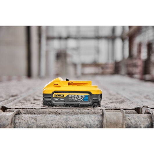 DEWALT POWERSTACK 18V 5Ah battery resting on a construction site surface.