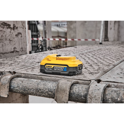 DEWALT POWERSTACK DCBP518 battery on a dusty construction site metal platform.