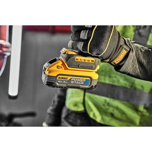 Gloved hand holding a DEWALT POWERSTACK 18V battery, close-up on the yellow and black product.