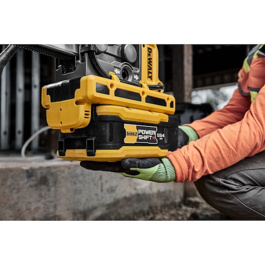 DEWALT Power Shift DCBPS0554 battery held by a worker in gloves at a construction site.