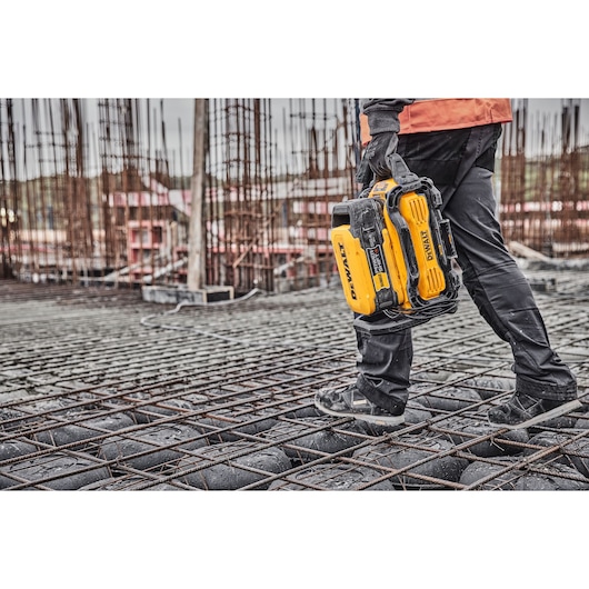 Person carrying a yellow DEWALT battery tool at a construction site with steel reinforcement and unfinished structures.