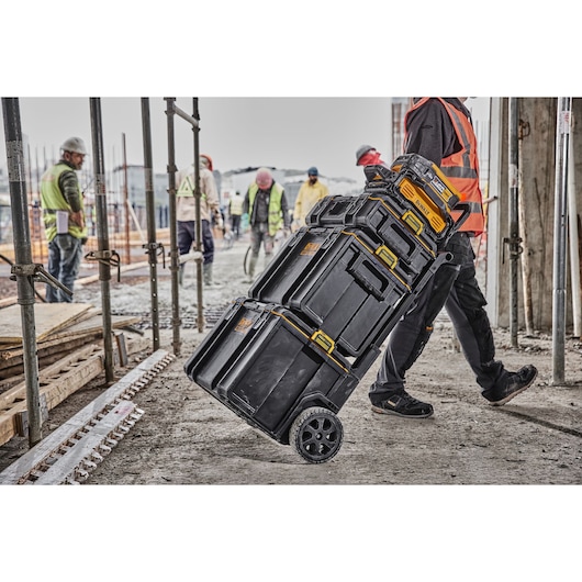 DEWALT wheeled toolboxes being rolled on a construction site by a worker in safety gear.