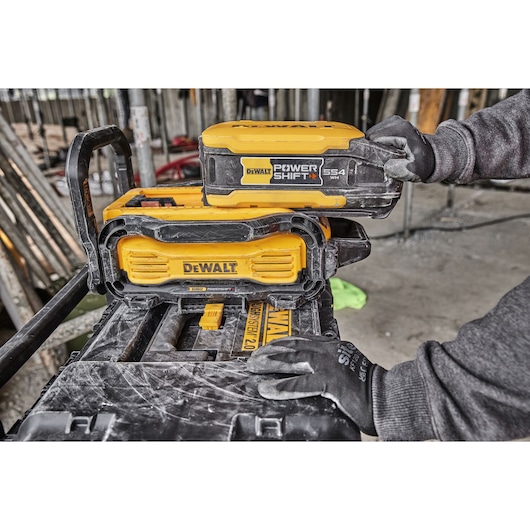 DEWALT PowerShift battery being placed on a yellow DEWALT charger, both used at a construction site.