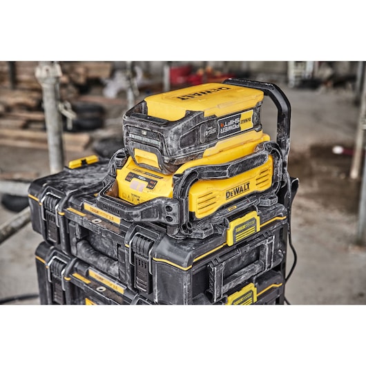 DEWALT battery charging station with stacked ToughSystem tool storage boxes, covered in dust, situated on a construction site.