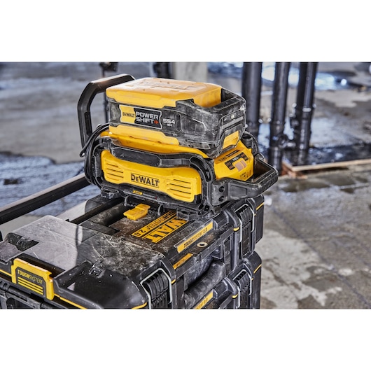 A DEWALT Power Shift 554 Wh battery and charger unit, attached to a DEWALT ToughSystem storage box, shown in a construction site setting.