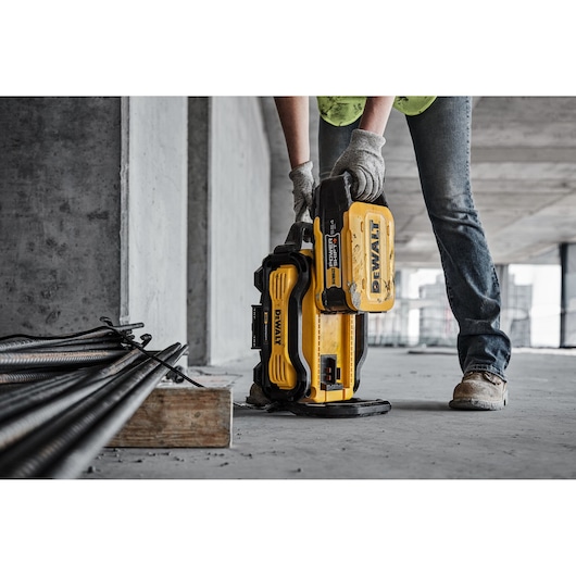 Person uses a yellow DEWALT battery pack on a construction site with tools and metal bars nearby.