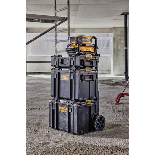 Stacked DEWALT ToughSystem toolboxes and organizers with wheels, standing on a construction site floor. The boxes are black with yellow accents and DEWALT branding.