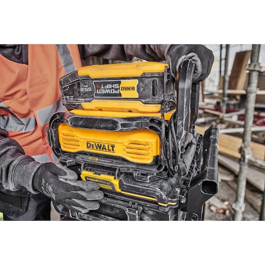 DEWALT Power Shift battery attached to TOUGHSYSTEM storage, worker in gloves on construction site.