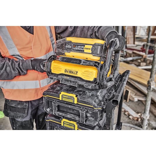 DEWALT ToughSystem toolboxes stacked, person in safety gear holding a yellow DEWALT PowerShift unit on top.