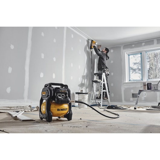 DEWALT cordless compressor used in a room under renovation, worker on ladder installing trim.