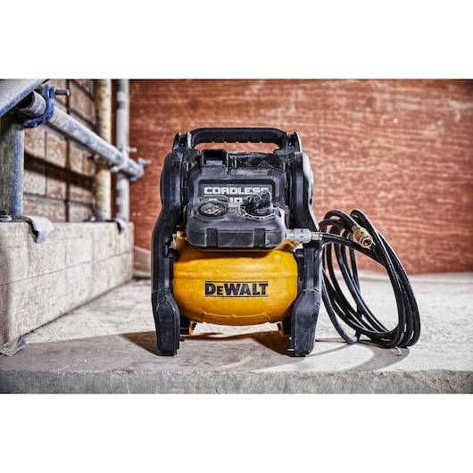 A DEWALT cordless air compressor with a yellow tank, black handle, control panel, and attached hose, positioned on a concrete surface in an industrial setting.