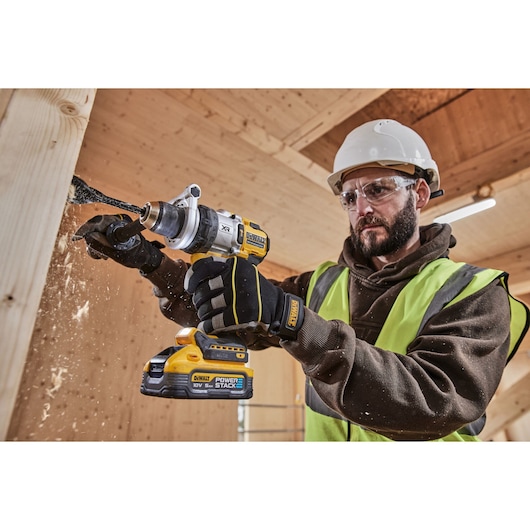 DEWALT cordless drill in use on wood, worker wearing gloves, helmet, and hi-vis vest in construction setting.