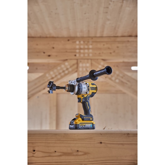DEWALT cordless drill with battery and side handle placed on wood, used for heavy duty drilling.