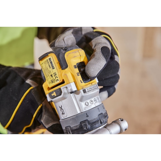 A gloved hand adjusts a yellow DEWALT cordless drill with visible labels and settings.