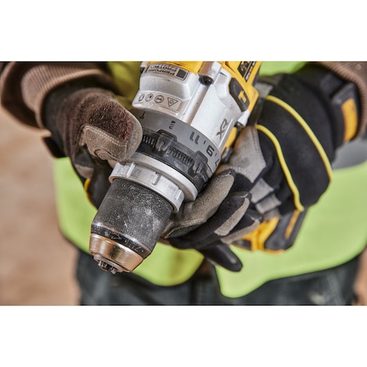 Gloved hands adjusting the chuck on a yellow DEWALT cordless drill at a construction site.