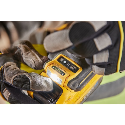 Gloved hands adjust controls on a yellow DEWALT tool with an illuminated LED light and visible settings icons.