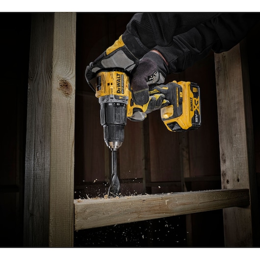 DEWALT cordless drill in use, drilling into wood with gloves on, wood shavings falling.