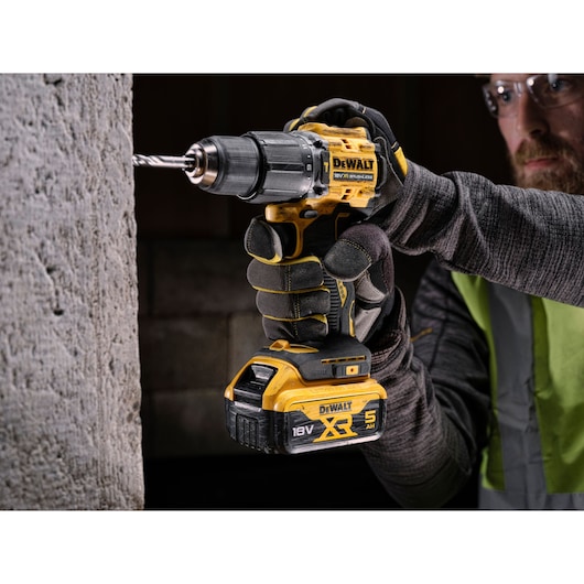 A DEWALT 18V XR cordless drill being used to drill into concrete, held by a gloved hand.