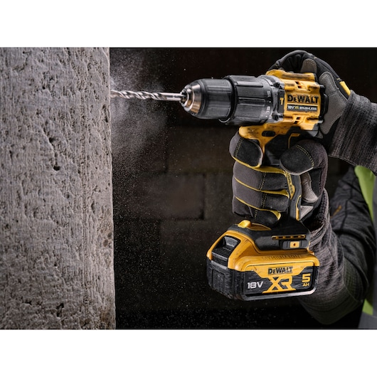 DEWALT cordless drill in use, drilling into concrete. Gloves and dust indicate active construction work.