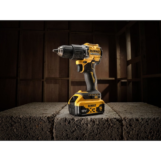 Cordless DEWALT power drill with 18V XR 5Ah battery, placed on concrete blocks in a workshop setting.