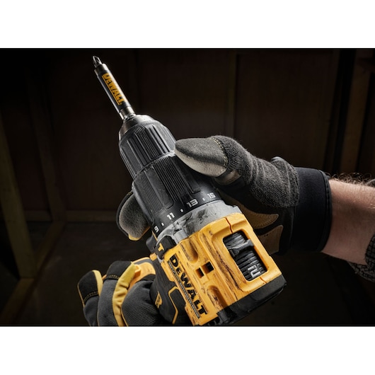Gloved hand holding a yellow and black DEWALT cordless drill inside a workshop.