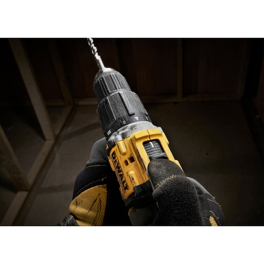 Gloved hand holding a yellow DEWALT cordless drill with a drill bit attached, indoors at a construction site.