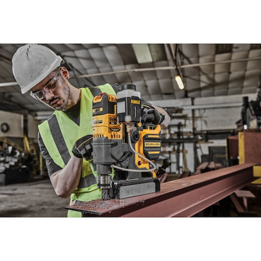 DEWALT DCD1623N brushless drill in use on metal beam in industrial workshop, operated by person in safety gear.