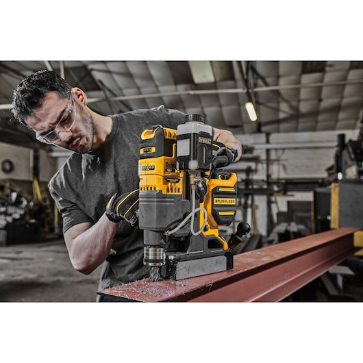 DEWALT DCD1623N brushless drill used on steel beam in workshop by person with face obscured.