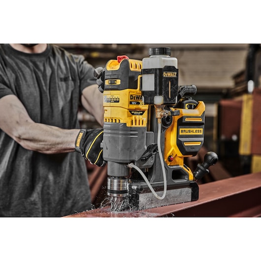 DEWALT brushless magnetic drill is used to bore a hole in a steel beam in an industrial workshop setting.