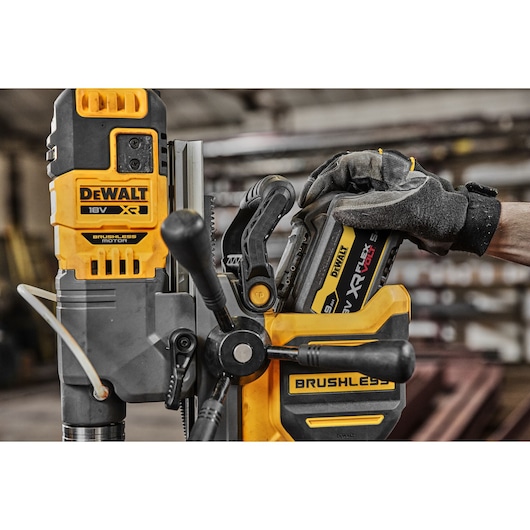 Hand inserting battery into yellow DEWALT cordless brushless drill in workshop setting.