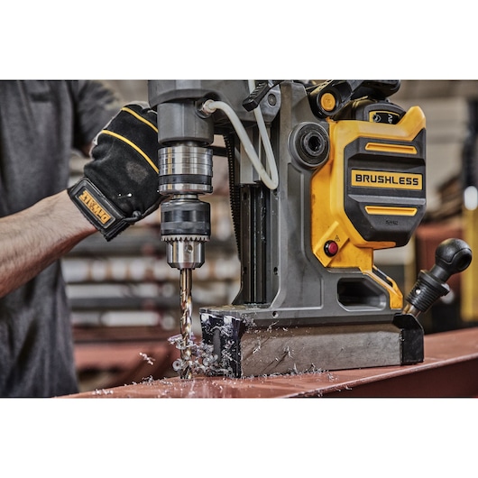 Person uses DEWALT brushless magnetic drill to bore holes in metal, creating metal shavings on a workshop table.