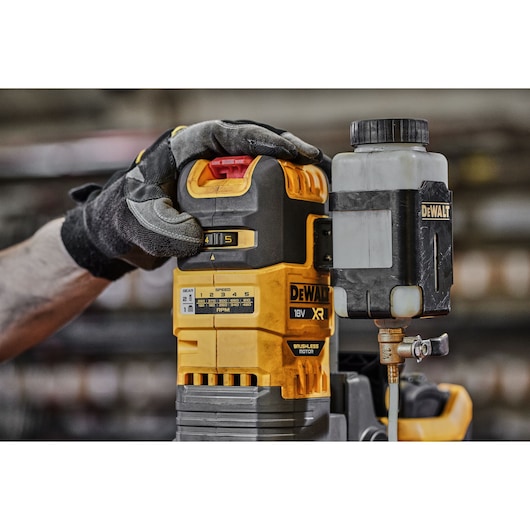 Gloved hand adjusts DEWALT DCD1623N cordless tool with lubricant tank in workshop setting.